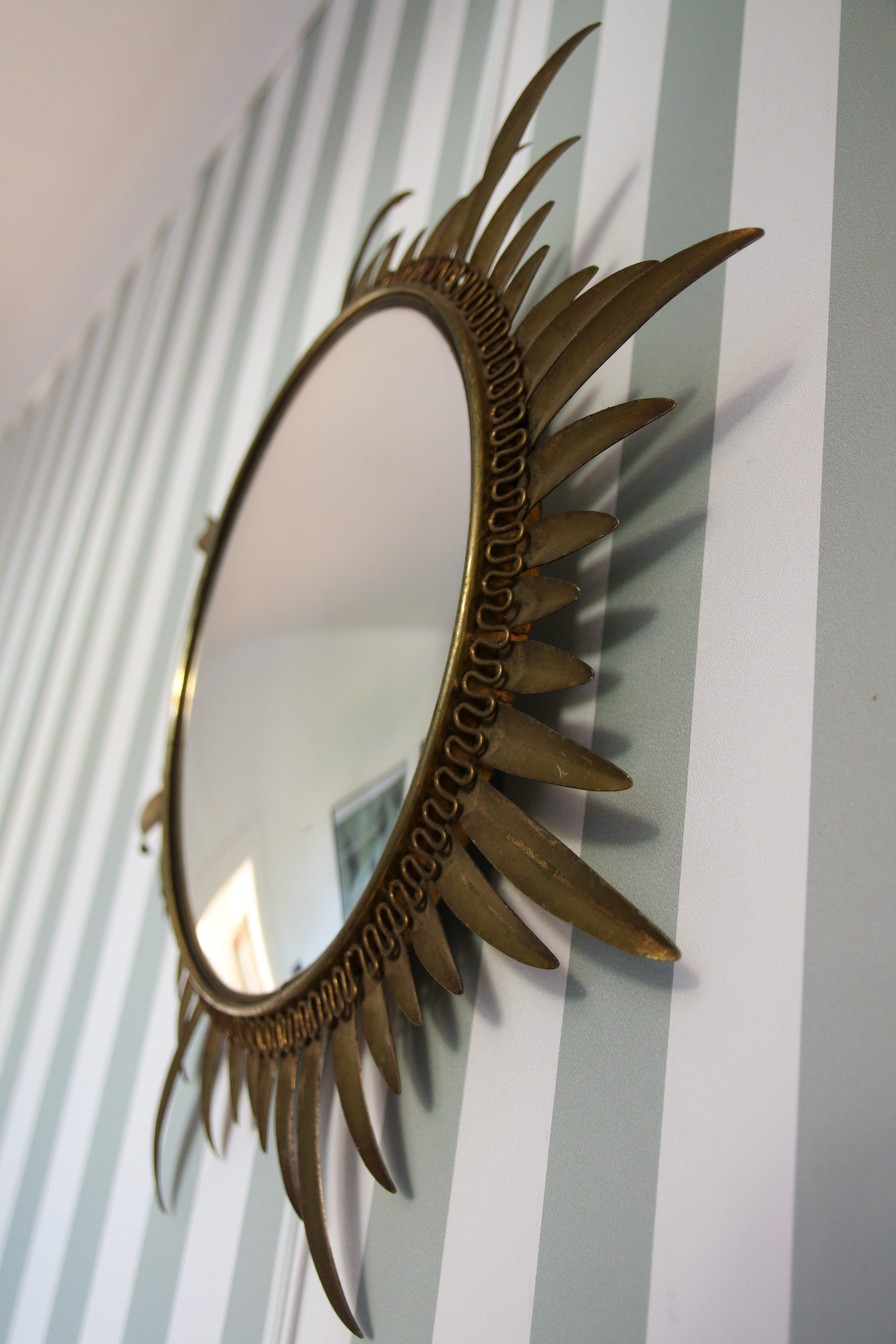 Gros plan sur un miroir de sorcière aux palmes, détail du cadre en métal doré patiné et du verre convexe, design vintage années 60, Studio Cinquante.