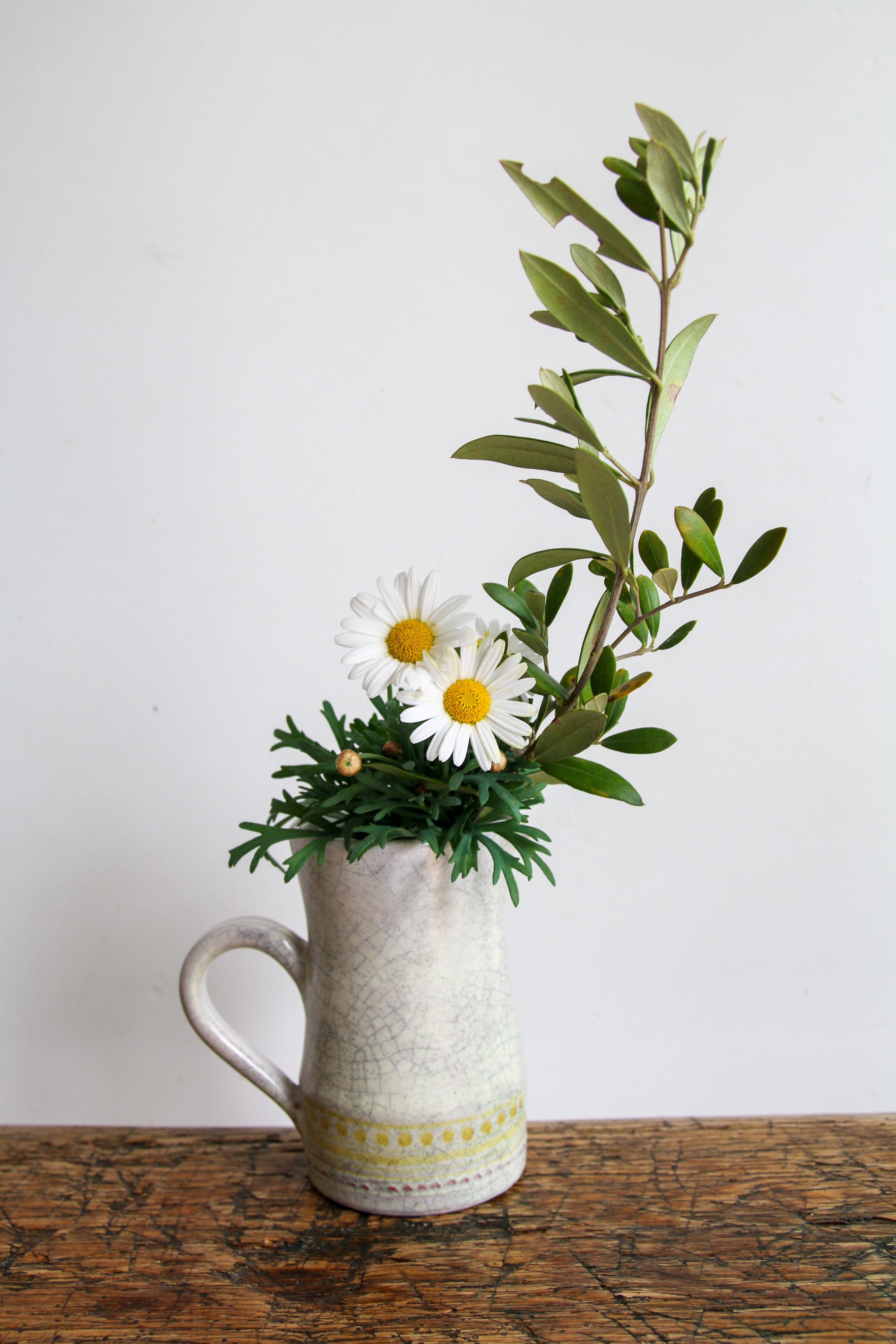 Vase pichet Roger Capron utilisé comme soliflore avec fleurs de camomille et branche d'olivier, design français après-guerre.